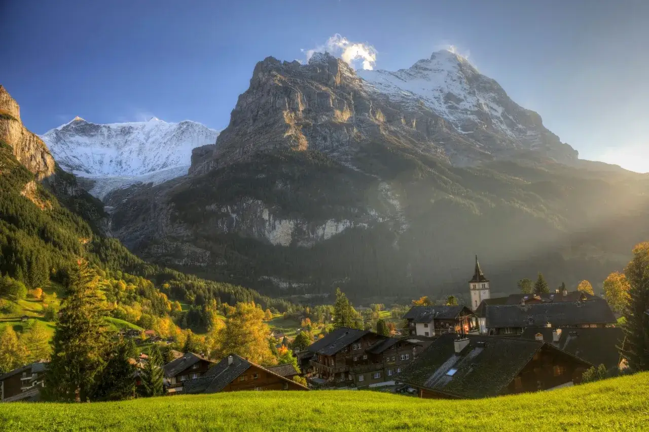 Malowniczy widok na Grindelwald, alpejską wioskę otoczoną ośnieżonymi szczytami i jesiennymi lasami.