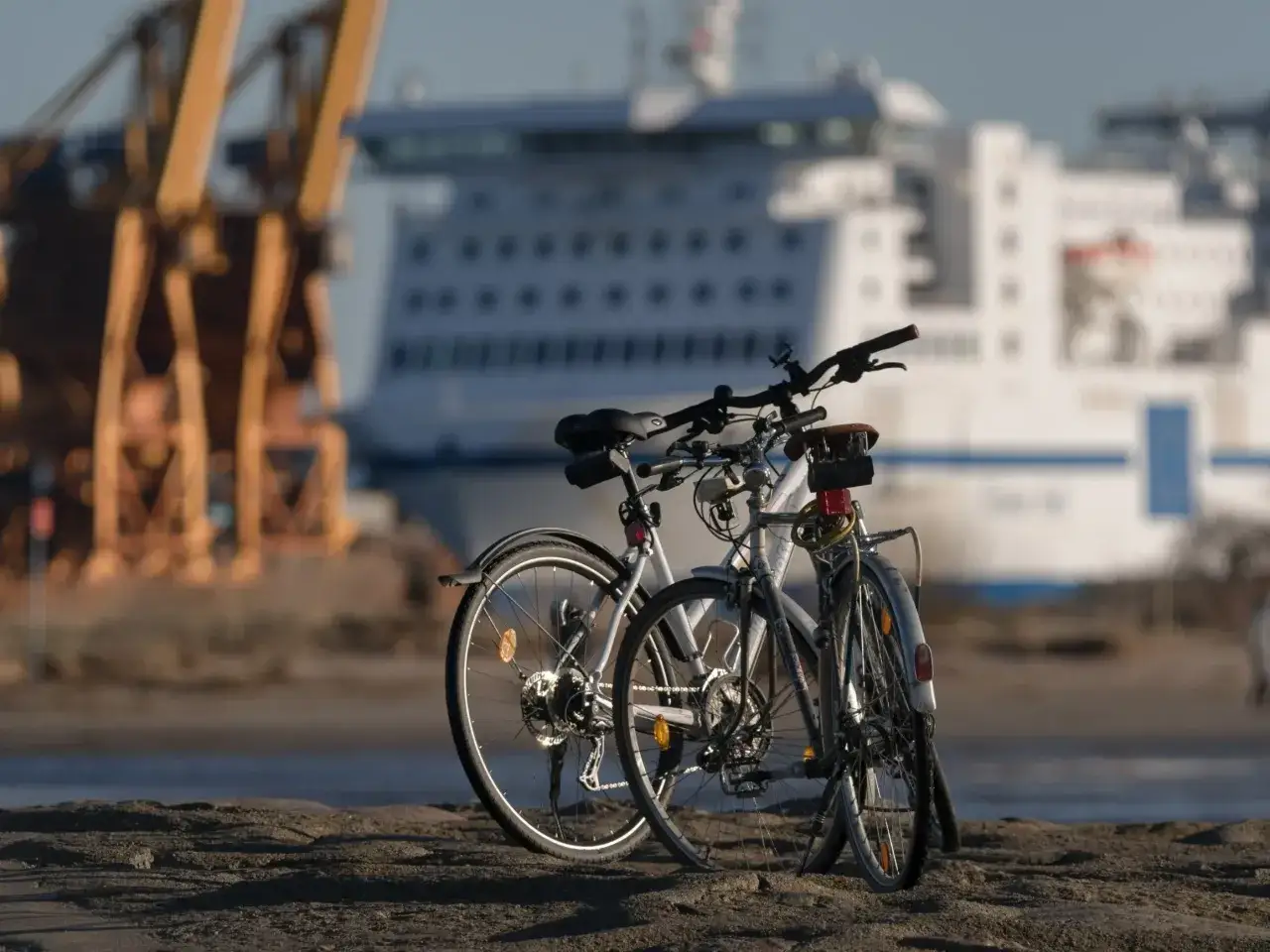 Dwa rowery czekają na odkrycie tras rowerowych nad morzem. W tle widać prom i portowe dźwigi.
