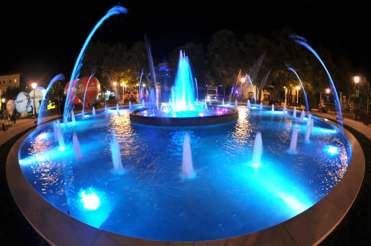 Krynica-Zdrój atrakcje wieczorem: podświetlana fontanna w centrum miasta, balony i drzewa w nocnej scenerii.