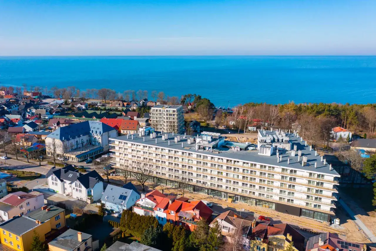 Widok z lotu ptaka na nadmorską miejscowość, gdzie leży Jarosławiec. Widać budynki mieszkalne, hotel i morze.
