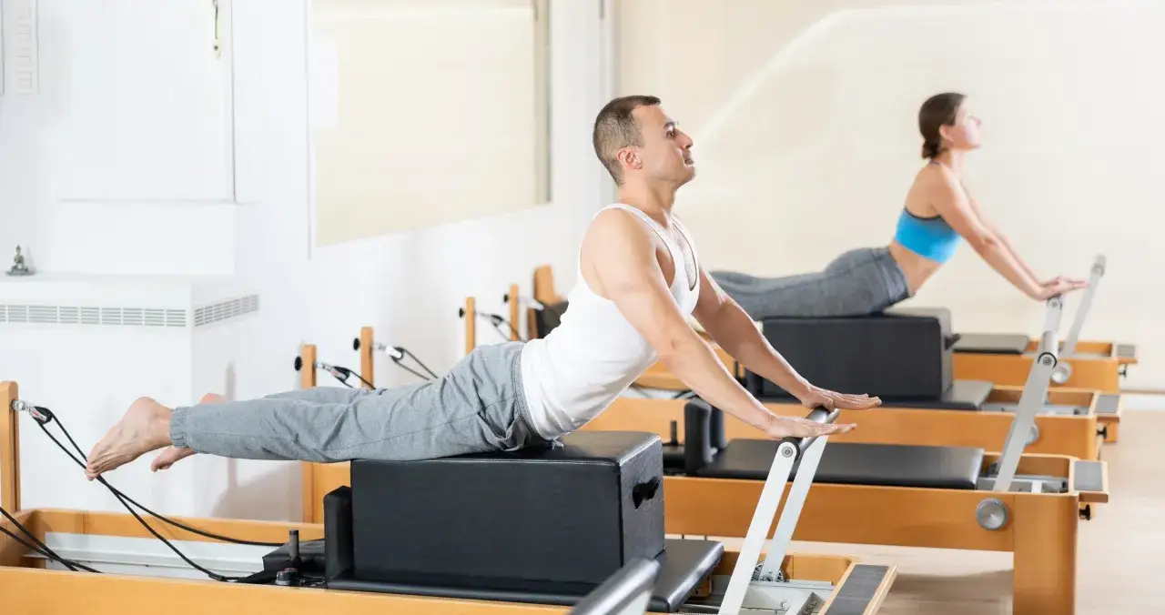 Mężczyzna i kobi ćwiczą na reformerach. To świetny sposób, by dowiedzieć się, pilates co to jest i jak poprawić sylwetkę.