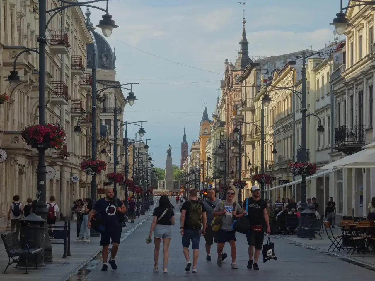 Spacerem po Piotrkowskiej w Łodzi, wśród kamienic i zieleni, ludzie cieszą się letnim dniem.