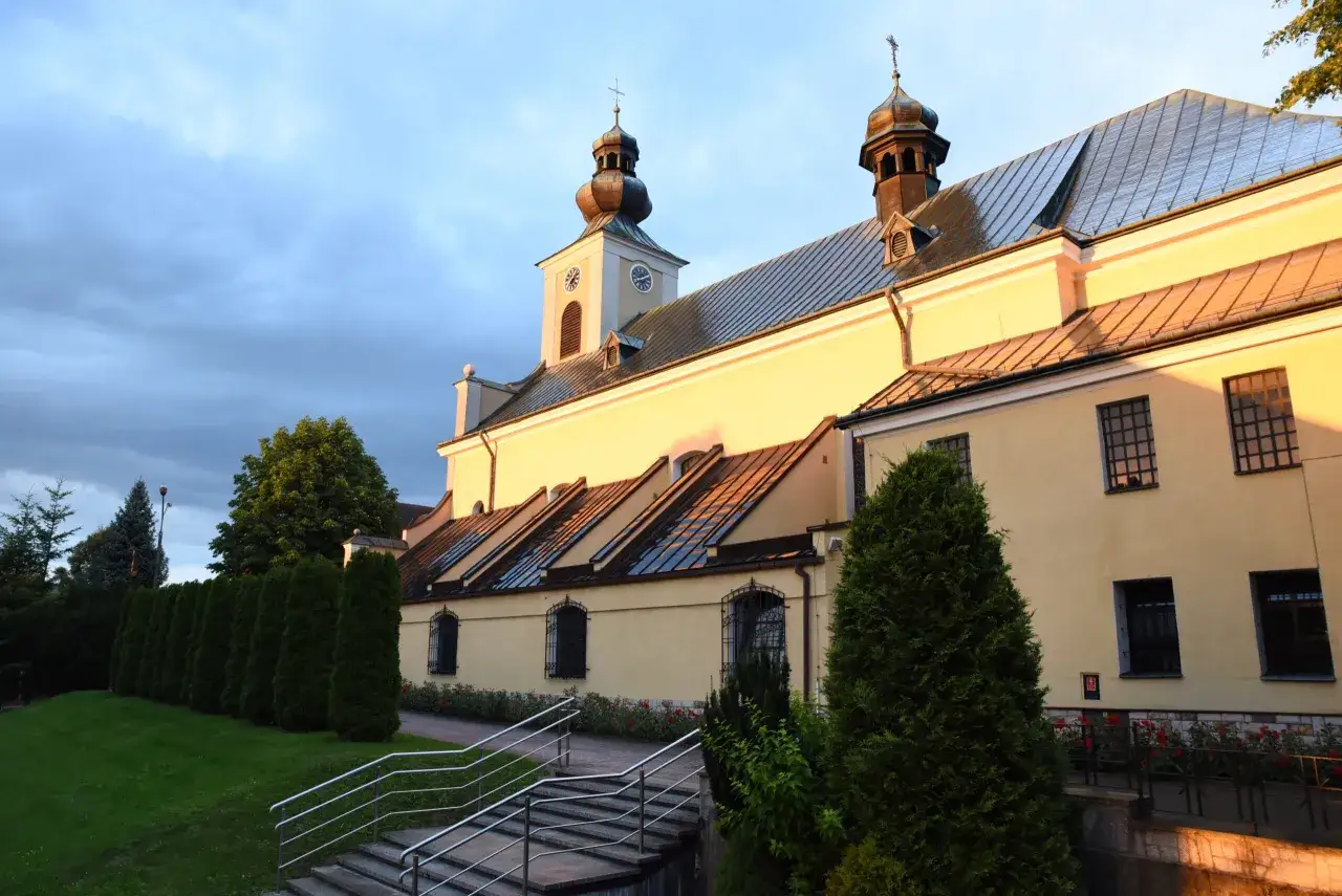 Kościół w Tymbarku oświetlony zachodzącym słońcem. W tle błękitne, zachmurzone niebo.