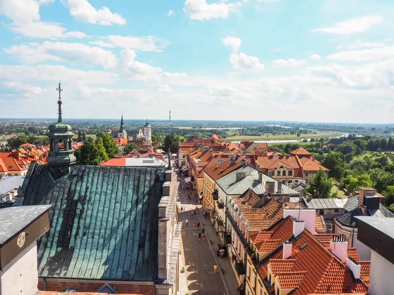 Widok na urokliwy sandomierz rynek z dachu kościoła. Kamienice z czerwonymi dachami, brukowana ulica i zielone wzgórza w tle.