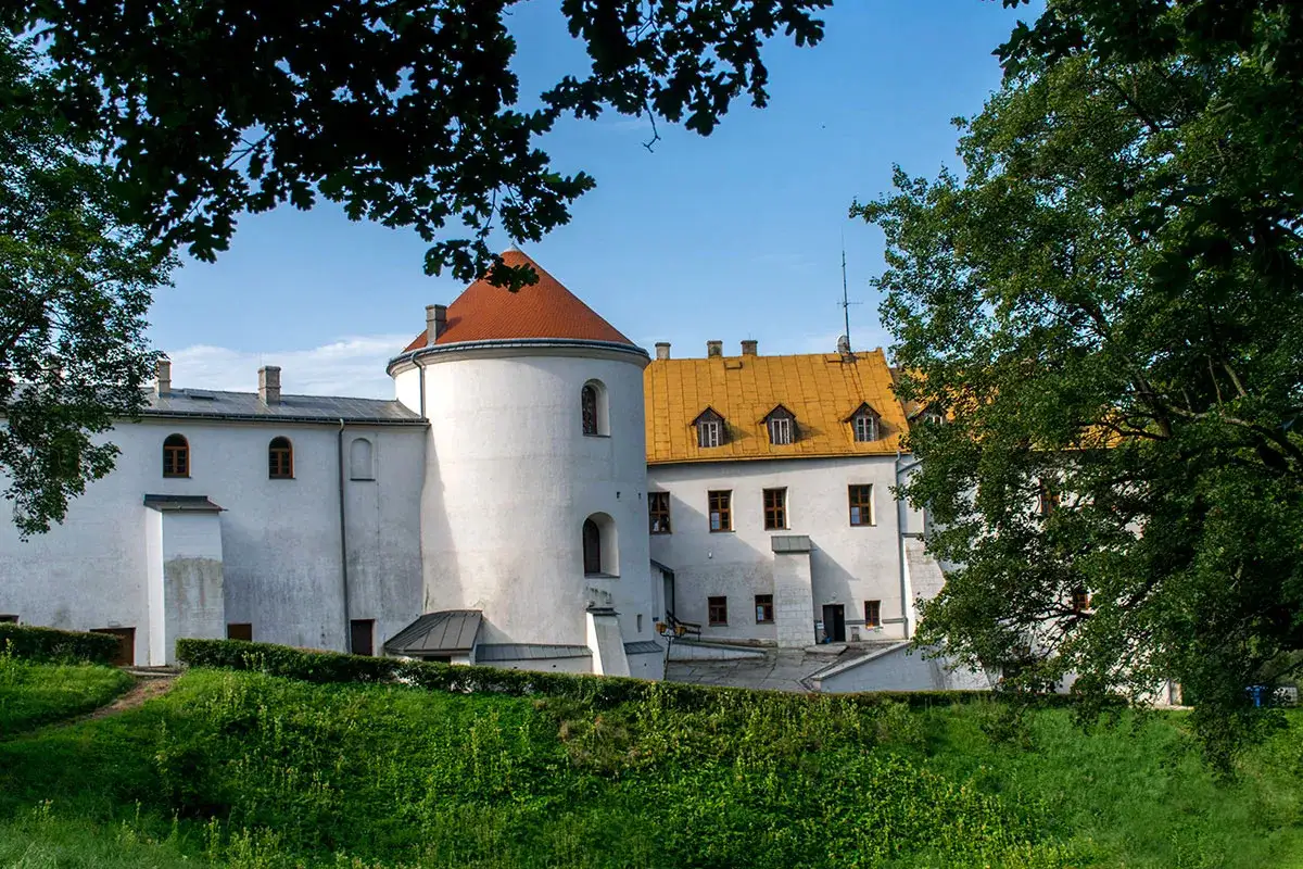 Zamek w Lesku, biała budowla z okrągłą wieżą i pomarańczowym dachem, otoczony zielenią.