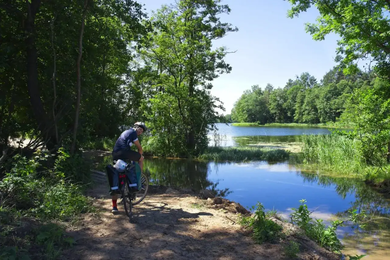 Rowerzysta odpoczywa nad jeziorem, podziwiając piękne trasy rowerowe Olsztyn.