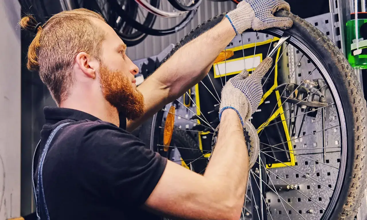 Mechanik w rękawiczkach naprawia rower, wyjmując dętkę z opony.