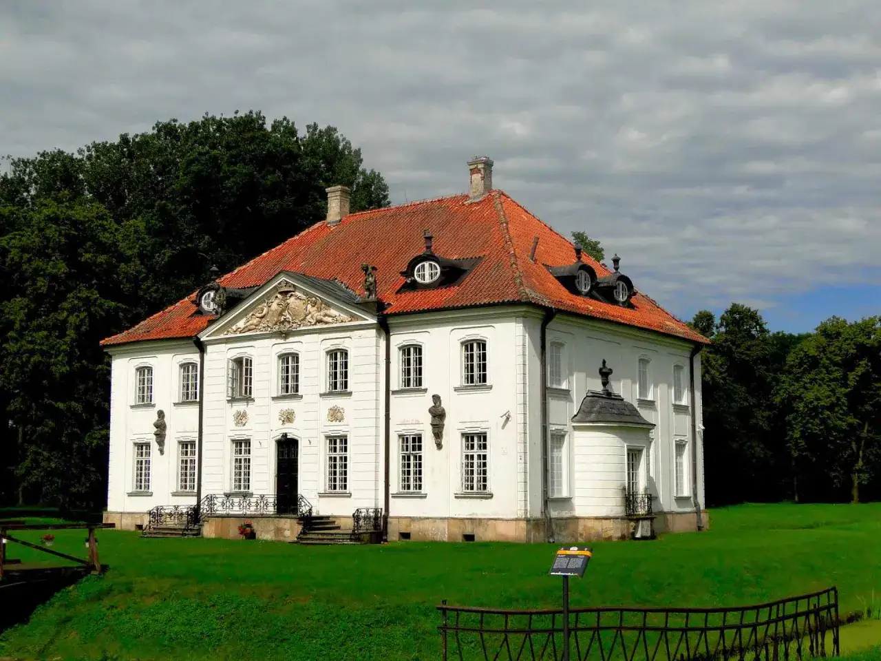 Pałac w Choroszczy, biała rezydencja z czerwonym dachem, otoczona zielenią.