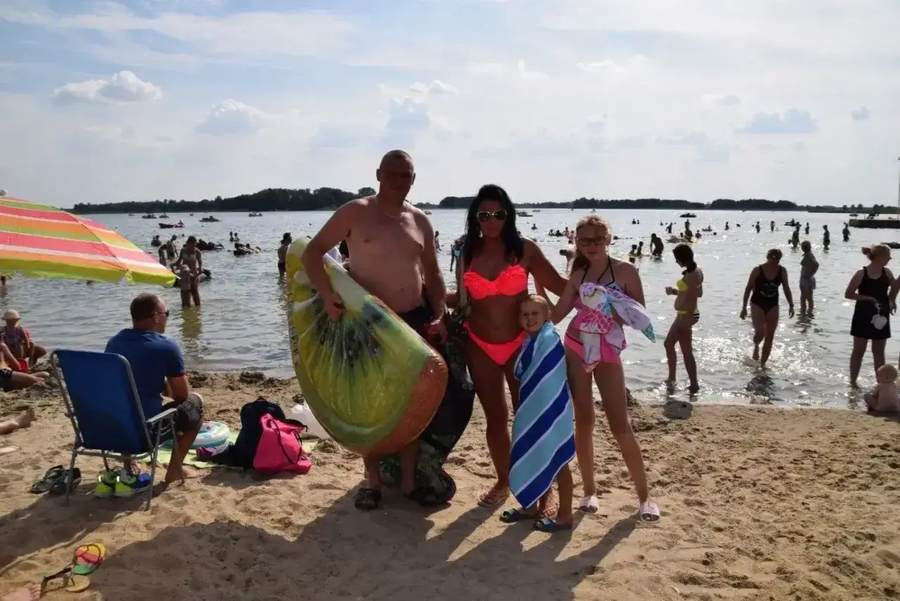 Rodzina na plaży w Skorzęcinie, ciesząca się słońcem i wodą. W tle mnóstwo ludzi i atrakcje wodne.