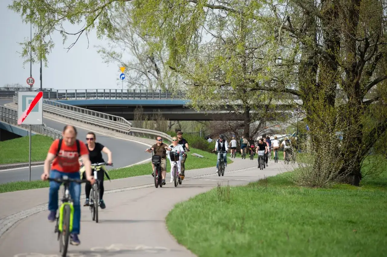 Ludzie jeżdżą na rowerach po malowniczej trasie rowerowej w Warszawie, ciesząc się wiosennym dniem.