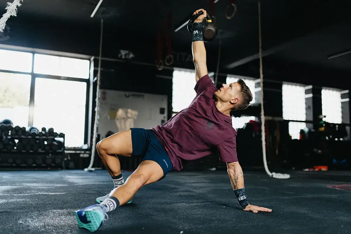 Mężczyzna wykonuje ćwiczenia gimnastyczne z kettlebell, unosząc go nad głowę.