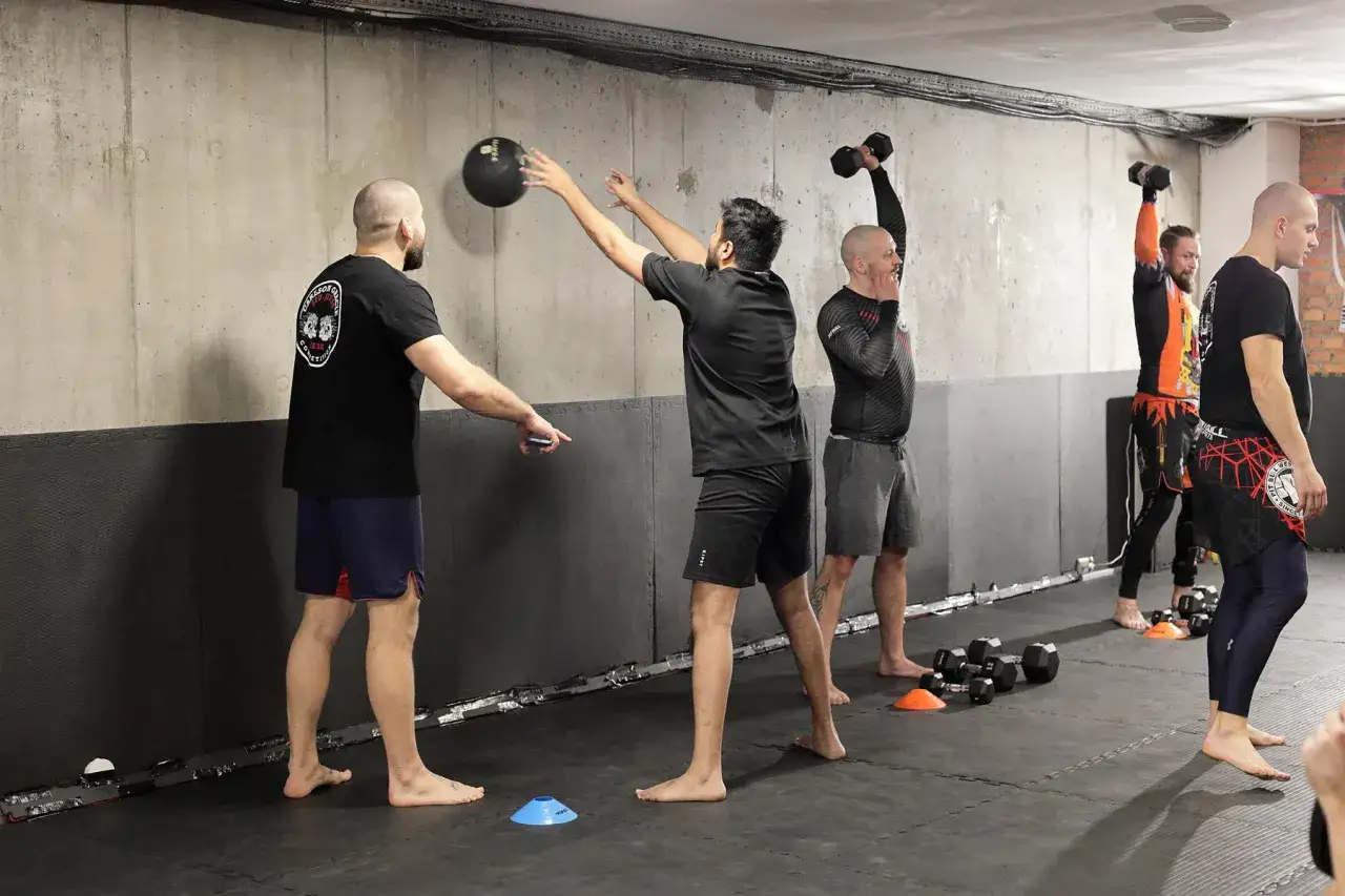 Trening crossfit we Wrocławiu: mężczyźni ćwiczą z piłką lekarską i hantlami na macie.