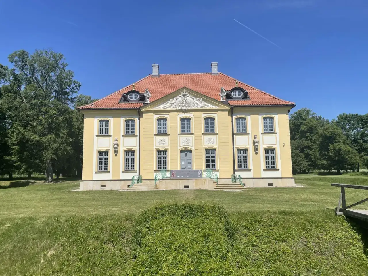 Pałac Branickich w Choroszczy, żółty, z czerwoną dachem, otoczony zielenią.