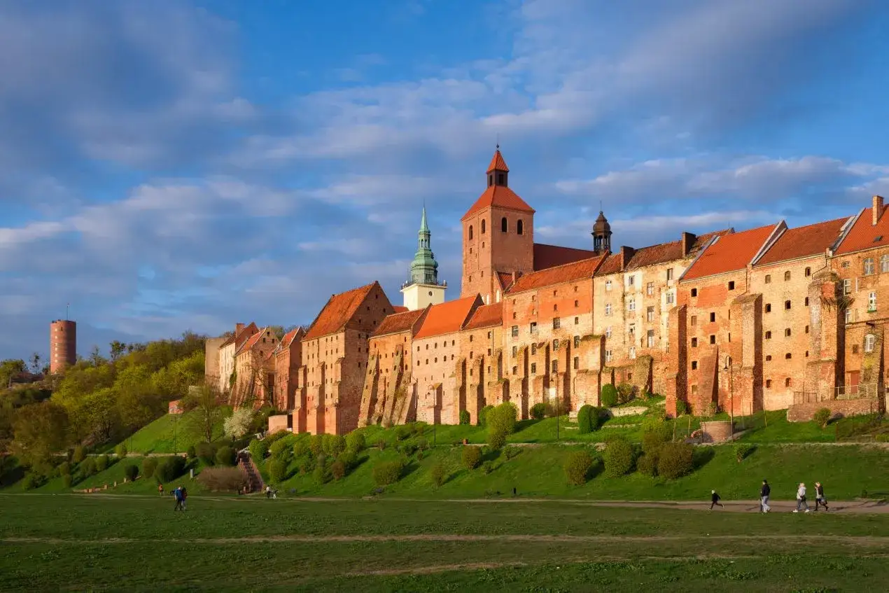 Imponujący grudziądz zamek z czerwonej cegły, z wieżami i dachami, na tle błękitnego nieba z chmurami.