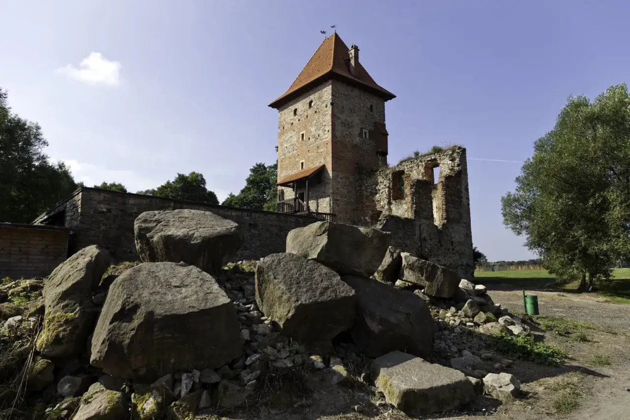 Ruiny zamku w Chudowie z wieżą i kamiennym murem, otoczone głazami i zielenią.