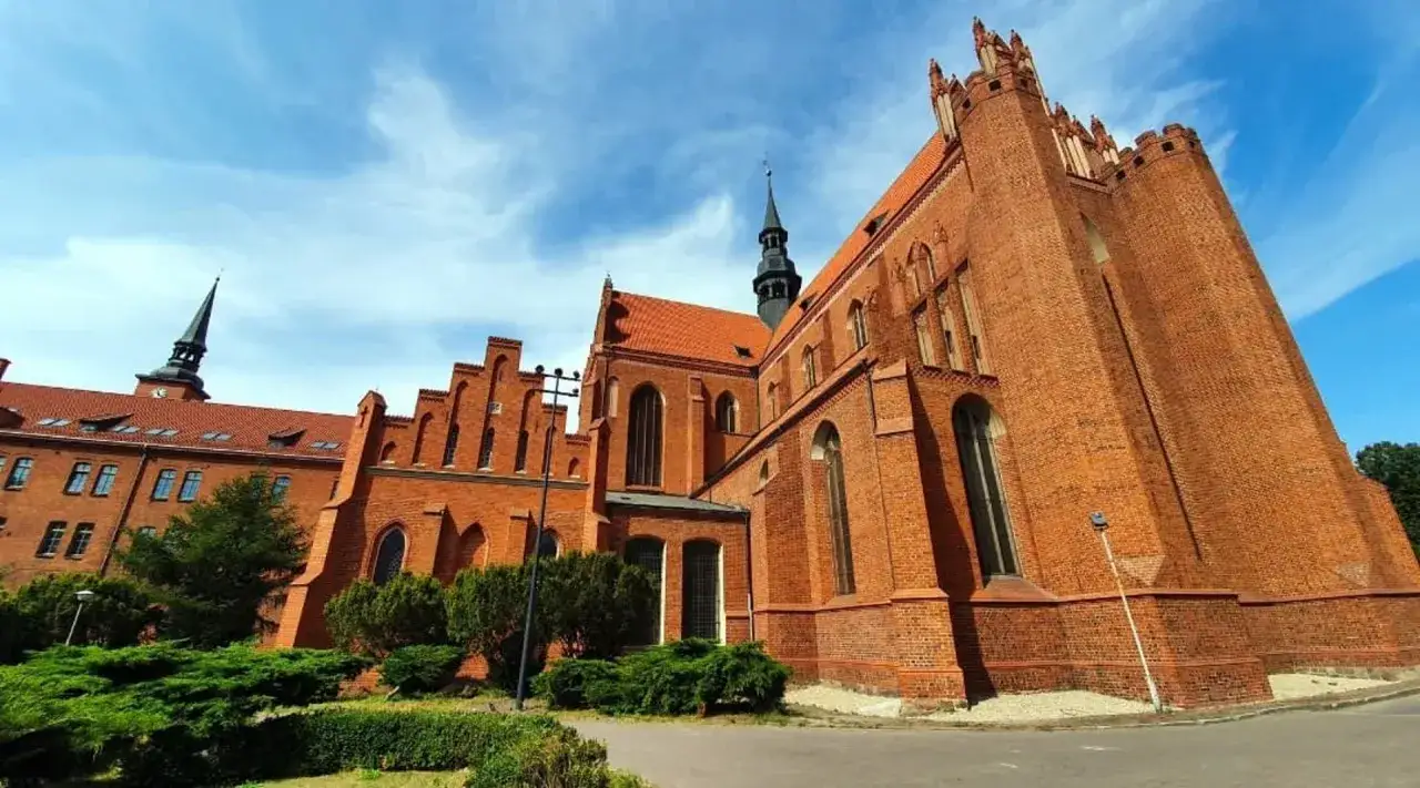 Gotycka ceglana katedra na Kociewiu, z charakterystyczną wieżą i zielenią wokół.