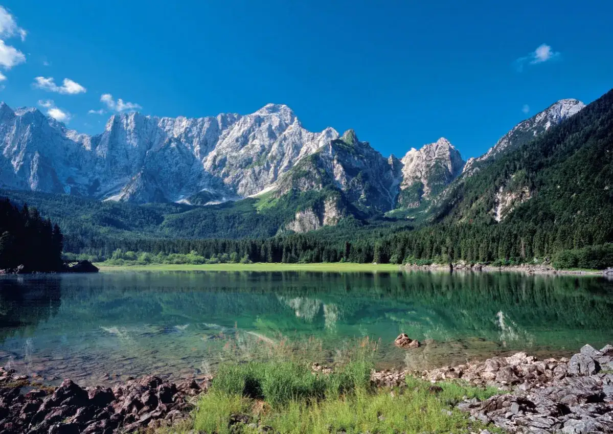 Spokojne jezioro odbija majestatyczne góry w pobliżu Tarvisio.