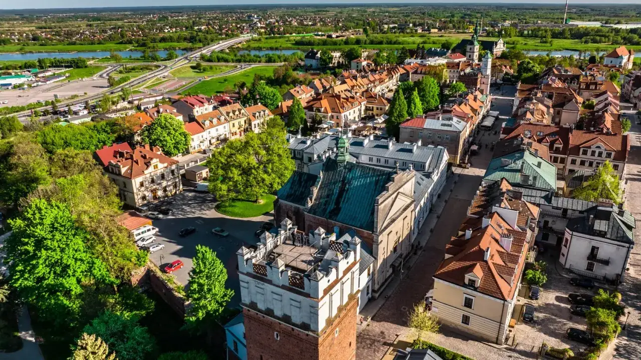 Widok z lotu ptaka na Sandomierz. Widać zabytkową wieżę, kamienice z czerwonymi dachami i fragmenty trasy widokowej.