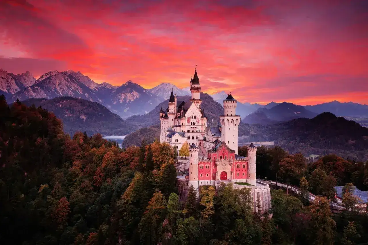 Bajkowy zamek Neuschwanstein, jeden z najpiękniejszych zamków w Niemczech, wznosi się na tle dramatycznego, czerwonego nieba i gór.